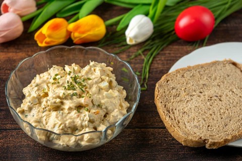 Egg salad next to a slice of bread and tulips, on rustic wooden table