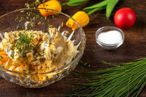 Chives fall into a bowl with ingredients for egg salad on wooden table