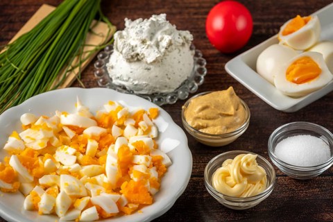 Sliced Easter eggs and fresh ingredients for a spread arranged on a wooden table