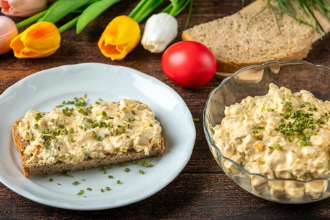 Slice of bread with egg salad on plate, with fresh herbs, tulips in the background
