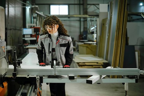 A person stands at a workbench in a workshop, preparing to cut wood. The space is filled with tools