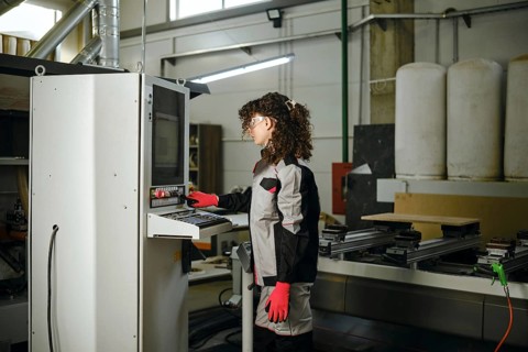 A person operates a milling machine in a carpentry workshop filled with tools and equipment. The
