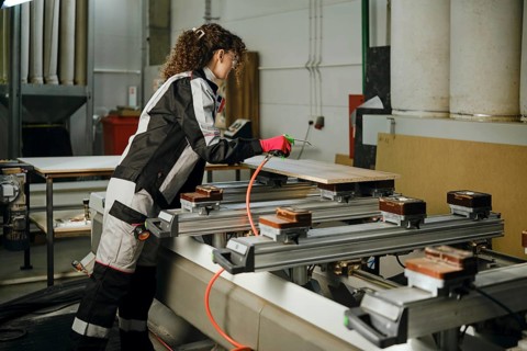 A worker blows away dust and shavings from the wooden panel using compressed air connected to a