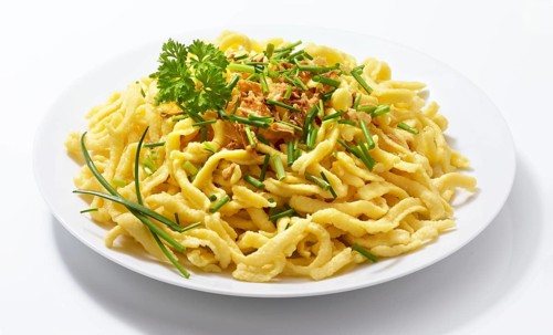 Plate with spaetzle decorated with roasted onions, chives and parsley, studio shot against a white