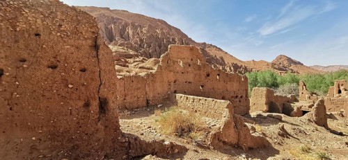 Ancient sandstone ruins in a dry, rocky landscape with sparse vegetation, Morocco