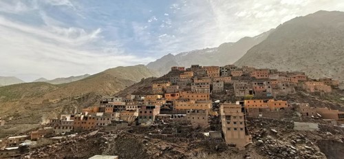 A mountainous village with many orange-colored houses in natural colors under a cloudy sky, Morocco