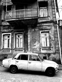 Monochrome, vintage car standing in front of a Nostaligian building with a distinctive balcony,