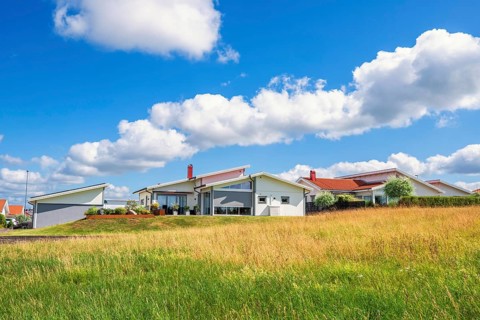 Modern residential houses with white facades and red roofs on grassy hillside under a blue sky with