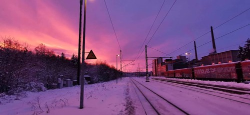 Sunrise at a snow-covered train station on Rennsteig, railroad tracks in purple sky with factory in