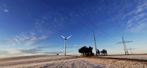 Winter landscape with wind turbine and power lines against a blue sky, Rennsteig, Frankenwald