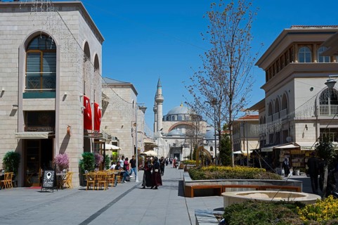 Lively shopping street with stylish buildings, mosque in the background and decorative lighting,