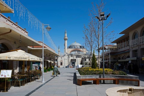 Wide pedestrian zone with shops and street cafés, a mosque in the background under a blue sky,