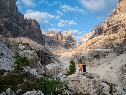 Two hikers in front of impressive mountain peaks of the Brenta Mountains, evening at Refugio