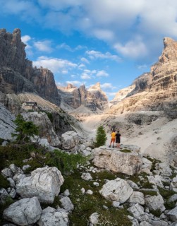 Two hikers in front of impressive mountain peaks of the Brenta Mountains, evening at Refugio