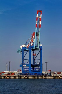 A single blue port crane, stacks of containers and a wind turbine in the background, The cranes of