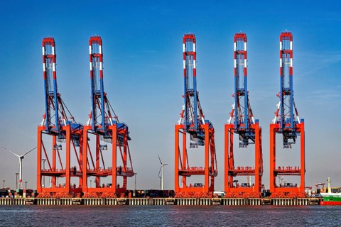 Set of red and blue cranes at the harbor, wind turbines and container warehouse in the background,