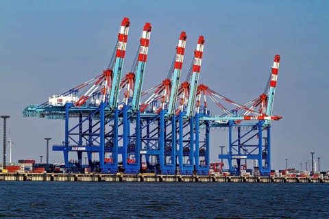Row of blue and red harbor cranes, containers in the background, calm water, The cranes of the