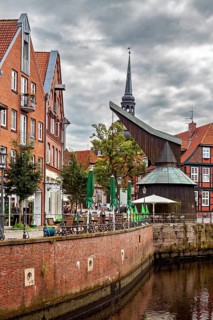 Timber crane and half-timbered houses with a tower on the riverbank under a dramatic sky, The old