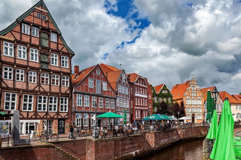 Half-timbered facades and terraces on the river with cyclists and cloudy sky, The old town of Stade