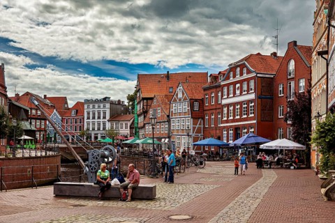 People sitting on cafe terraces along the river under a cloudy sky, The old town of Stade