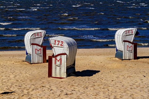 There are three white beach chairs with red numbers on the quiet and sandy beach with waves, beach