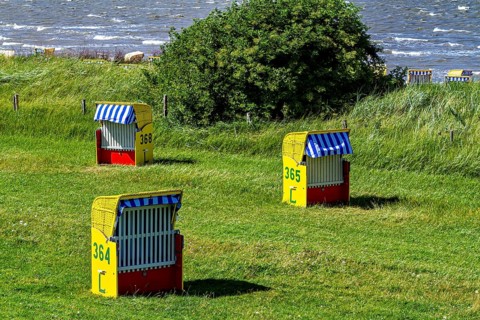 Three colorful beach chairs on a green grassy area with a view of the sea, beach chairs on the