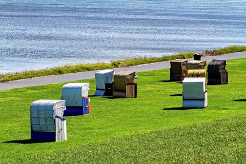 Beach chairs in different colors in a meadow next to a waterside road, beach chairs on the beach in