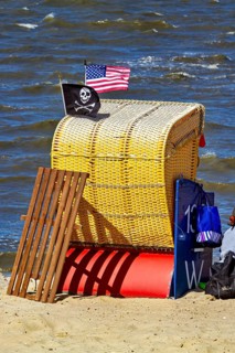 A single yellow beach chair on the beach with American and pirate flag in the wind, beach chairs on