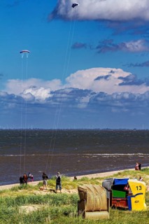 Beach chairs by the sea with people and kites in the sky under blue sky and clouds, beach chairs on