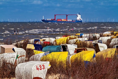 Beach chairs on the beach with a ship on the sea and wind turbines on the horizon, beach chairs on