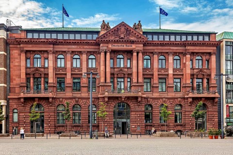 Historic bank building with red façade and two flags on the roof under a blue sky, The center of