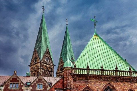 Gothic church towers with green roofs rise against a dramatic cloudy sky, The center of the