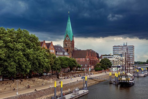 City landscape with a church, its Gothic tower and boats on the waterfront under a cloudy sky, The
