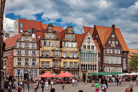 Half-timbered houses in a historic old town. People stroll across a busy market square in cloudy
