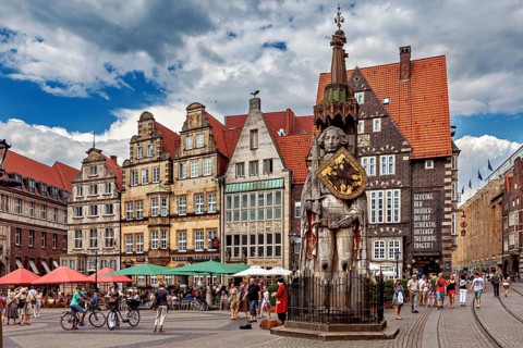 Lively city center with an impressive statue in front of historic buildings under a partly cloudy