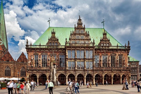 Impressive Renaissance building with green roof and statue, people walking in changeable weather,