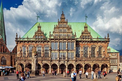 A historic Renaissance-style building on a busy market square in Bremen, under a cloudy sky, The