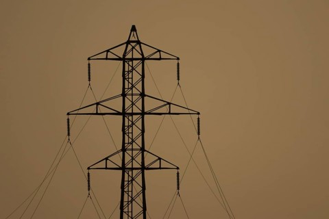 Electricity pylon and power lines silhouette at sunset, England, United Kingdom