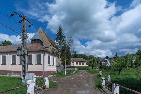 Village street with abandoned 16th century Lutheran fortified church in Tobsdorf, Romanian Dupus,