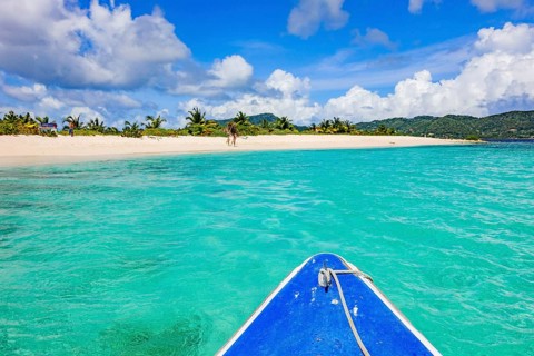 View of blue bow from small tour boat onto turquoise blue-green lagoon in front of uninhabited