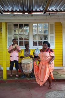 Guatemalan woman in traditional dress singing and dancing, men playing music in the back, Garifuna