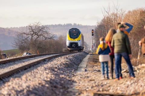 People watch a train traveling on a railway line in rural surroundings, fire brigade exercise at