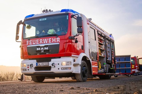 A fire engine with an open equipment door on a street in the morning light, ready to be deployed,