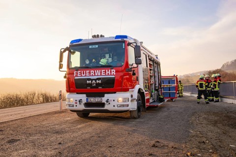 Firefighters stand by a fire truck on the side of the road at sunrise, ready for action, fire
