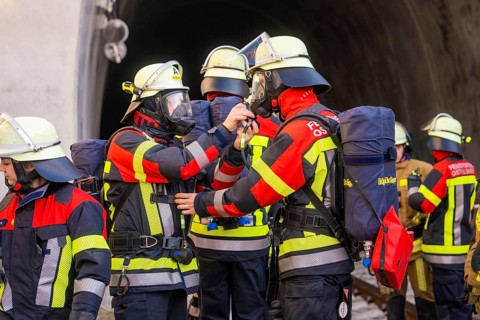 Firefighters in protective clothing deployed in front of a tunnel, focused on communication tasks,