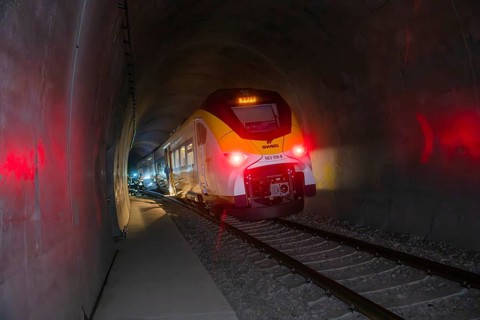 Modern train passes through illuminated tunnel breaking through darkness, fire brigade exercise on