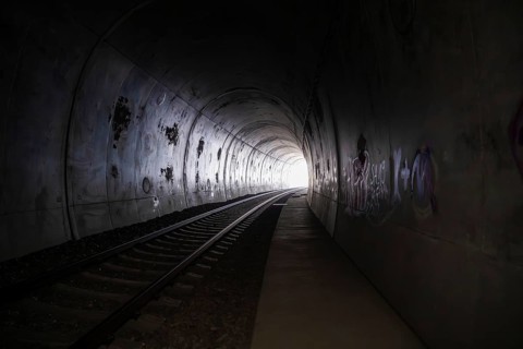 Dark tunnel with railroad tracks, graffiti and a light in the distance, fire brigade exercise on