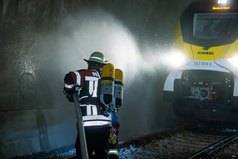 Firefighter with hose and respirator in front of a train in a tunnel, fire department exercise on