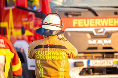 A firefighter stands in front of a fire truck wearing protective clothing, fire department exercise
