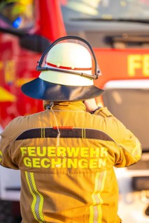 A firefighter stands in front of a fire truck wearing protective clothing, fire department exercise